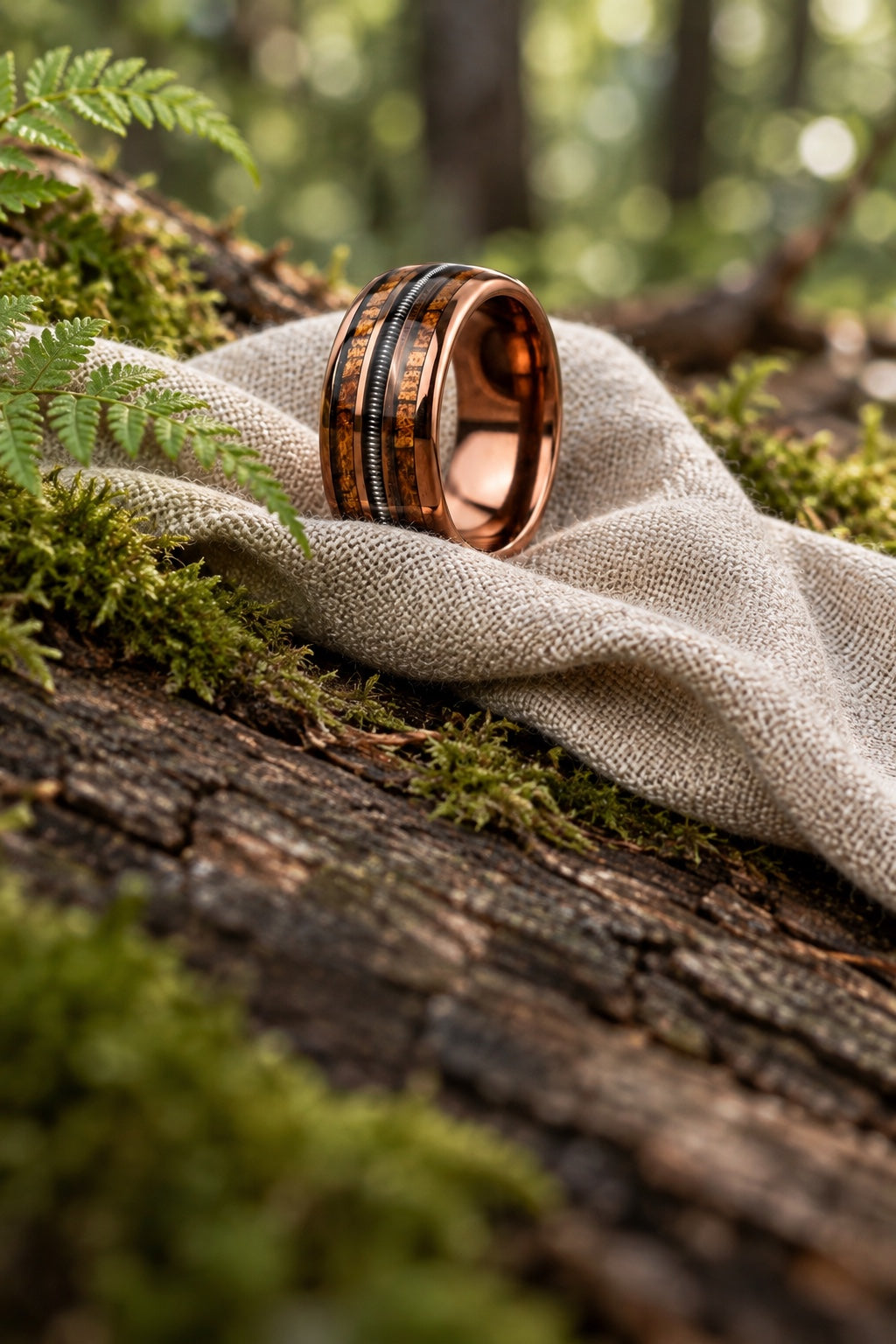 Rose gold wood and guitar string wedding band resting on linen among woodland moss and ferns
